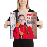 An eye safety poster of a young woman wearing safety glasses and orange gloves smiling as she works in a warehouse with a safety slogan in the top right corner.