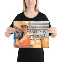 A workplace safety poster showing a young warehouse worker in a yellow hardhat and orange reflective vest holding a clipboard and smiling with the slogan safety is everyone's responsibility.