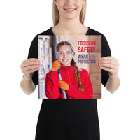 An eye safety poster of a young woman wearing safety glasses and orange gloves smiling as she works in a warehouse with a safety slogan in the top right corner.