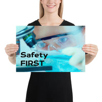A safety poster showing a close up of a lab worker's eyes examining a sample on a microscope while wearing safety glasses and a mask with the slogan safety first in bold letters.