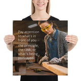 Workplace safety poster of a young female woodworker wearing safety glasses and gloves and sanding a two by four in her shop with a safety quote to the left.