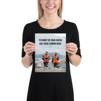 A safety poster showing two workers in reflective vests collaborating on a construction site with the proverb to know the road ahead ask those coming back.