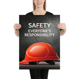 A workplace safety poster showing a red hard hat in front of a grey, industrial-looking background with the slogan safety is everyone's responsibility.