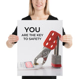 A workplace safety poster showing a lockout tagout lock and tag with the text you are the key to safety.