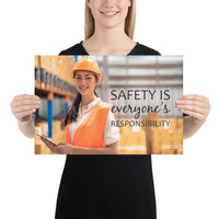 A workplace safety poster showing a young warehouse worker in a yellow hardhat and orange reflective vest holding a clipboard and smiling with the slogan safety is everyone's responsibility.