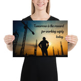 A safety poster showing a worker on a construction site being silhouetted by a sunset of orange and blue colors with the slogan tomorrow is the reward for working safely today.