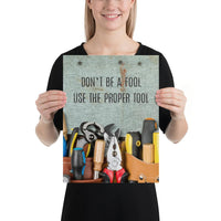 A workplace safety poster showing various tools such as a screwdriver, wrench, and pliers on a wooden table with the slogan don't be a fool use the proper tool.