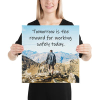 A workplace safety poster showing a man standing on a peak of a mountain with a bright blue sky and mountains behind him with the slogan tomorrow is the reward for working safely today.
