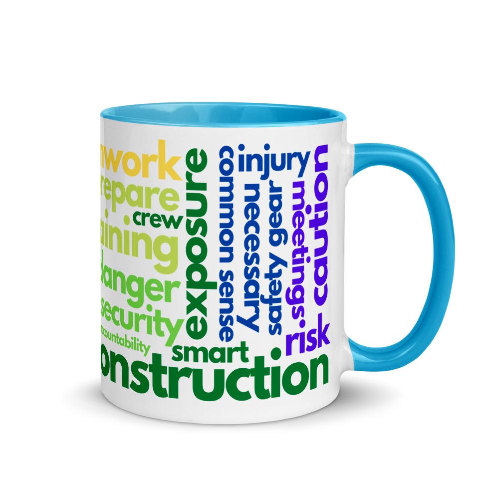 White ceramic mug with safety terms like hard hats, protection, and encourage, in a rainbow pattern across the mug with a blue rim, inside, and handle.