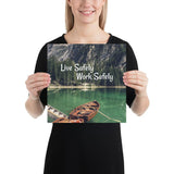 A workplace safety poster depicting a beautiful landscape of mountains in the background of a lake with a little wooden boat in the lake with text saying live safely work safely.
