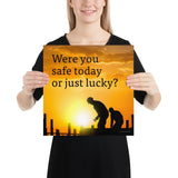A workplace safety poster showing workers on a construction site being silhouetted in black with a sunset of orange hues in the background with the slogan were you safe today, or just lucky?