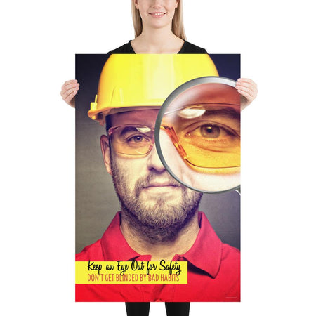 A workplace safety poster showing a portrait of a man wearing a hardhat and safety glasses with a magnifying glass magnifying one eye with the slogan, keep an eye out for safety, don't get blinded by bad habits.
