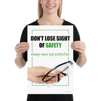 An eye safety slogan showing a close up of a hand presenting out safety glasses with a safety slogan in blue text above.