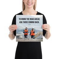 A safety poster showing two workers in reflective vests collaborating on a construction site with the proverb to know the road ahead ask those coming back.