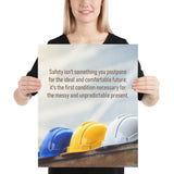 A workplace safety poster showing 3 multi colored hardhats sitting on a wall with the slogan safety isn't something you postpone for the ideal and comfortable future. It's the first condition necessary for the messy and unpredictable present.