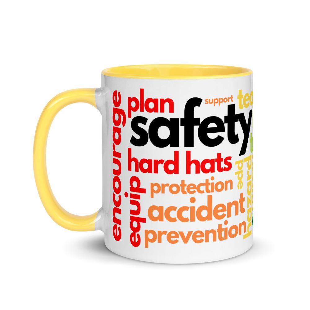 White ceramic mug with safety terms like hard hats, protection, and encourage, in a rainbow pattern across the mug with a yellow rim, inside, and handle.