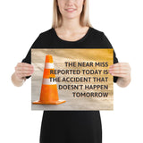 A workplace safety poster showing an orange safety cone with the slogan the near miss reported today is the accident that doesn't happen tomorrow.