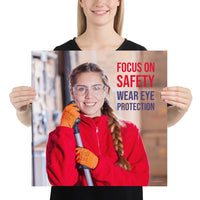 An eye safety poster of a young woman wearing safety glasses and orange gloves smiling as she works in a warehouse with a safety slogan in the top right corner.
