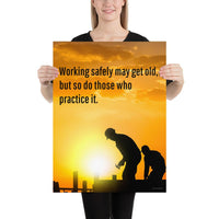 A workplace safety poster showing a construction site and construction workers being silhouetted by a bright and beautiful sunset of different shades of orange with the slogan working safely may get old, but so do those who practice it.
