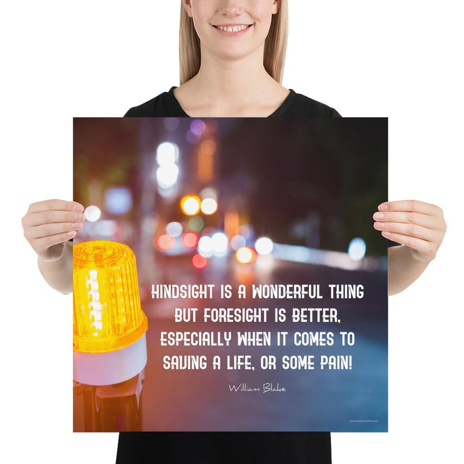 A workplace safety poster depicting a bright orange construction traffic light in the foreground of a blurry nighttime cityscape with a safety quote by William Blake.