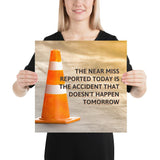 A workplace safety poster showing an orange safety cone with the slogan the near miss reported today is the accident that doesn't happen tomorrow.