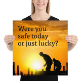 A workplace safety poster showing workers on a construction site being silhouetted in black with a sunset of orange hues in the background with the slogan were you safe today, or just lucky?