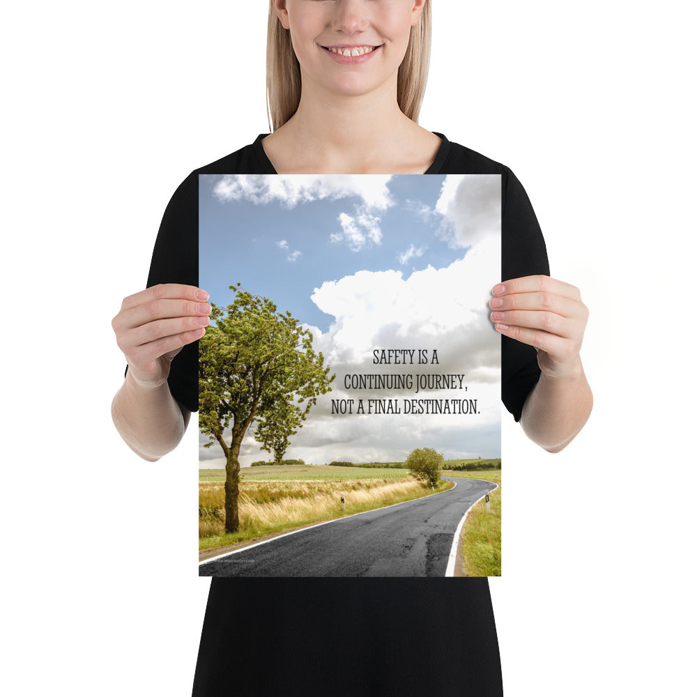 A workplace safety poster depicting a beautiful sunny day with a bright blue sky and a lush green field being cut down the middle by a road leading off into the countryside with the text safety is a continuing journey, not a final destination.