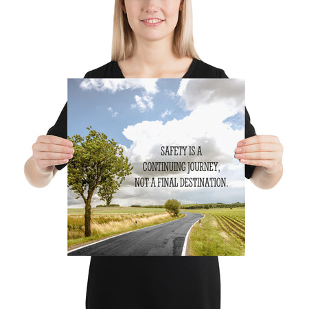 A workplace safety poster depicting a beautiful sunny day with a bright blue sky and a lush green field being cut down the middle by a road leading off into the countryside with the text safety is a continuing journey, not a final destination.