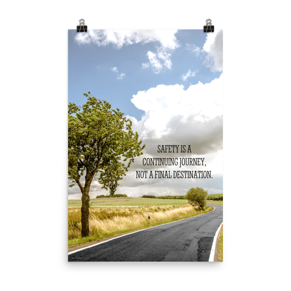 A workplace safety poster depicting a beautiful sunny day with a bright blue sky and a lush green field being cut down the middle by a road leading off into the countryside with the text safety is a continuing journey, not a final destination.