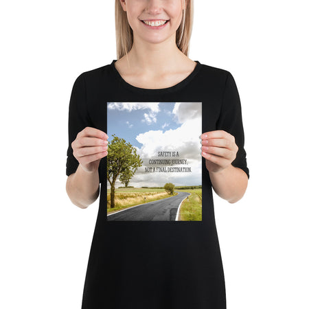 A workplace safety poster depicting a beautiful sunny day with a bright blue sky and a lush green field being cut down the middle by a road leading off into the countryside with the text safety is a continuing journey, not a final destination.