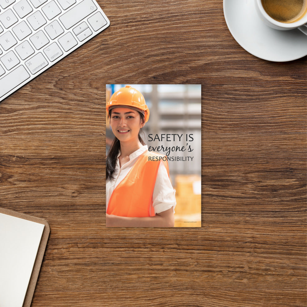 A workplace print showing a young warehouse worker in a yellow hardhat and orange reflective vest holding a clipboard and smiling with the slogan safety is everyone's responsibility.