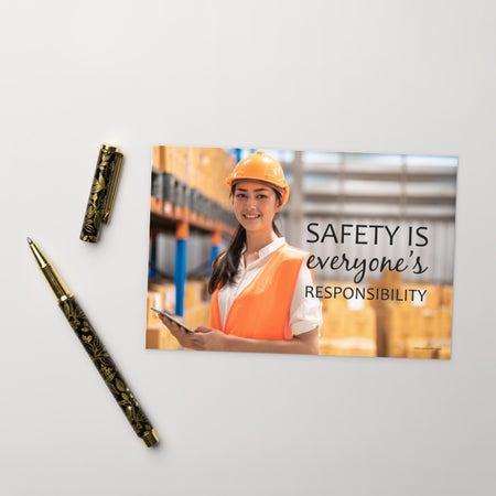 A workplace print showing a young warehouse worker in a yellow hardhat and orange reflective vest holding a clipboard and smiling with the slogan safety is everyone's responsibility.