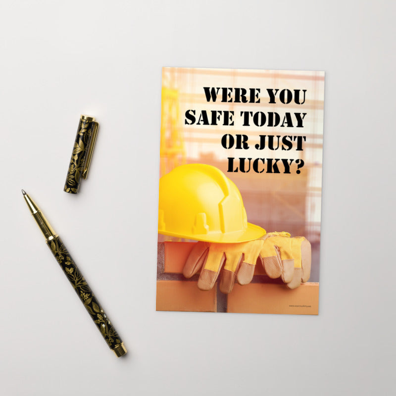 A workplace safety print showing a yellow hard hat and some gloves sitting on a brick wall on a construction site with the slogan were you safe today, or just lucky written in black stencil font.