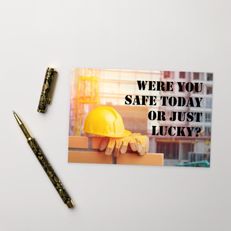 A workplace safety print showing a yellow hard hat and some gloves sitting on a brick wall on a construction site with the slogan were you safe today, or just lucky written in black stencil font.