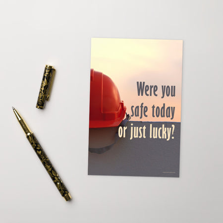 A workplace safety print showing a red hard hat sitting on a grey wall with a dreamy sunset background and the slogan were you safe today, or just lucky?
