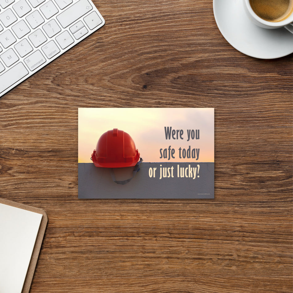 A workplace safety print showing a red hard hat sitting on a grey wall with a dreamy sunset background and the slogan were you safe today, or just lucky?