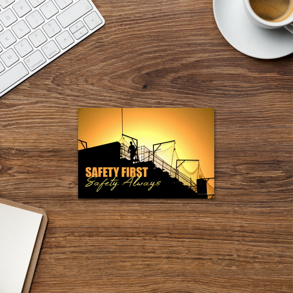 A workplace safety print showing a construction site and construction workers being silhouetted by a bright and beautiful sunset of different shades of orange with the slogan safety first, safety always.