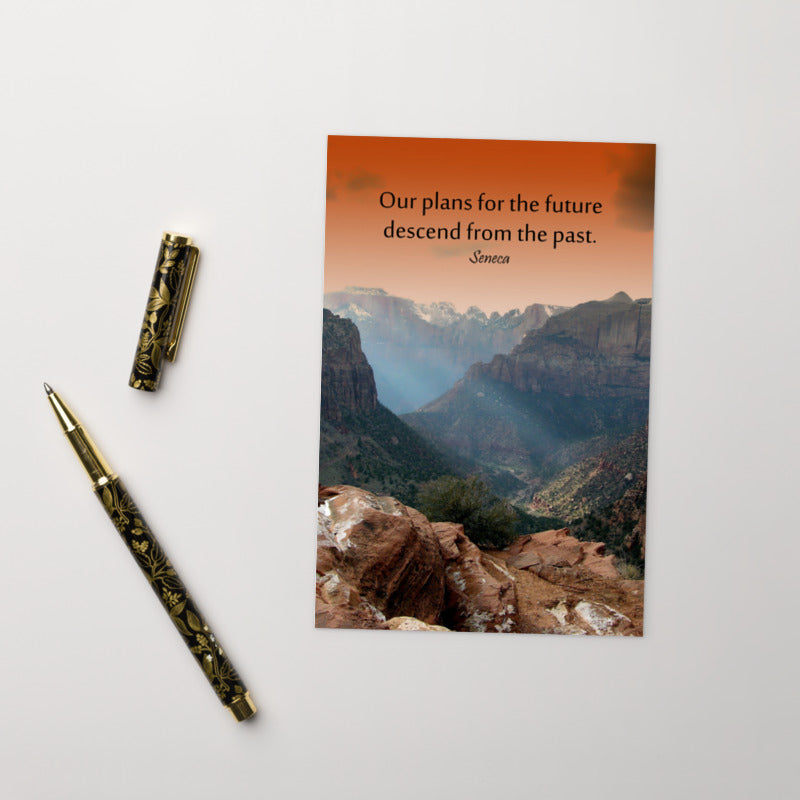 A safety print showing a landscape of burnt orange tinted mountains with the sunlight piercing through the tops of the mountains with the quote our plans for the future descend from the past by Seneca.