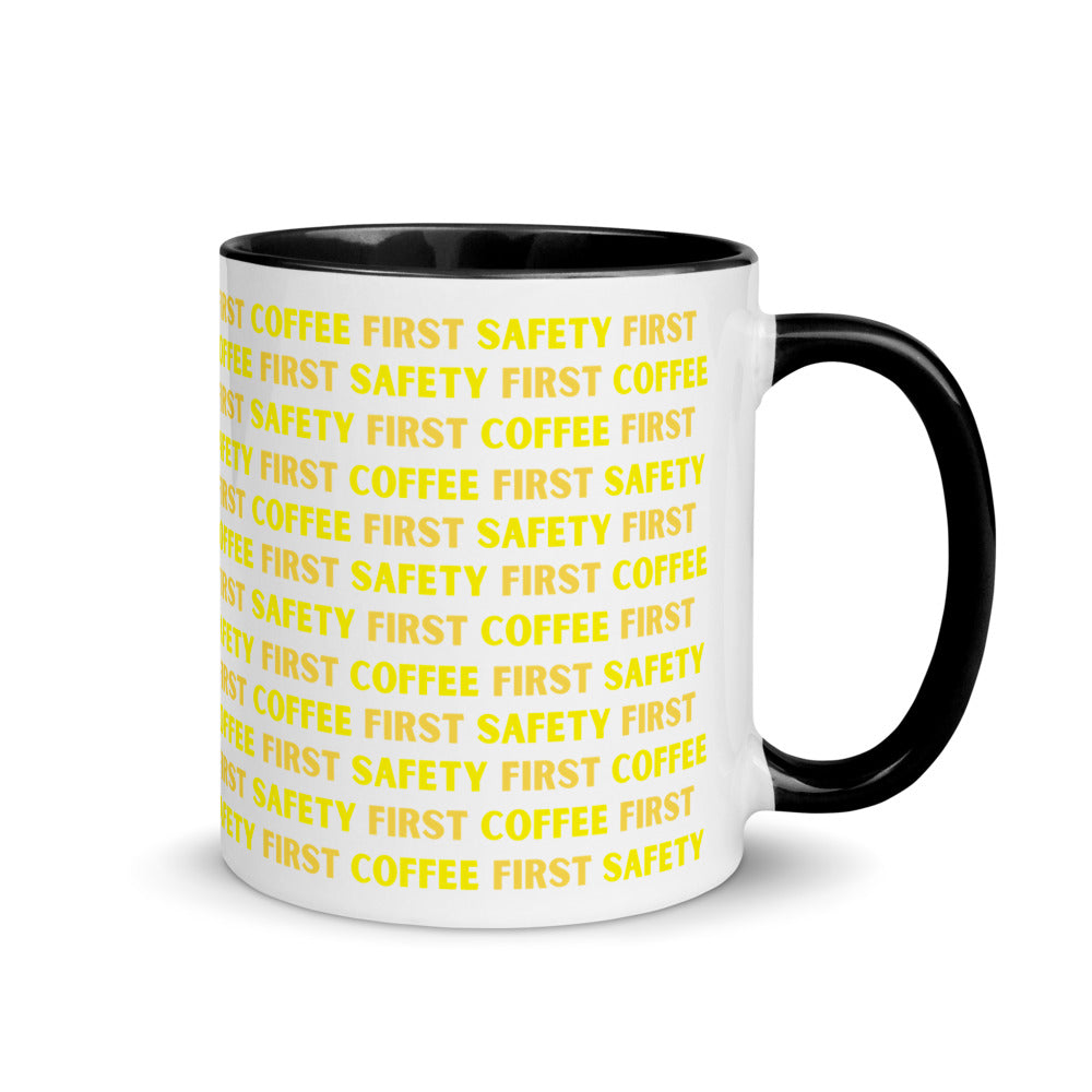 White ceramic mug with yellow repeating text that says "Safety First, Coffee First" with a black rim, inside, and handle.