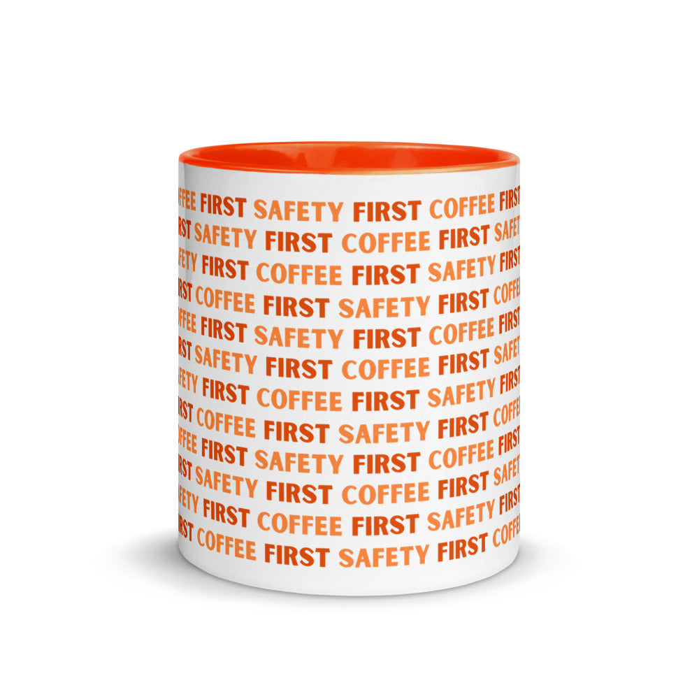 White ceramic mug with orange repeating text that says "Safety First, Coffee First" with an orange rim, inside, and handle.