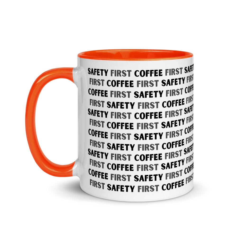 White ceramic mug with black repeating text that says "Safety First, Coffee First" with a orange rim, inside, and handle.