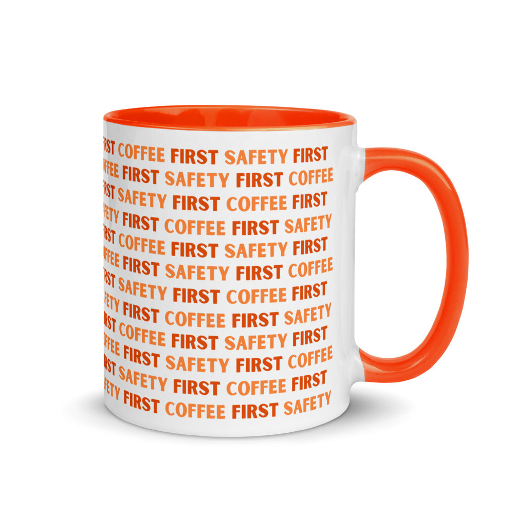 White ceramic mug with orange repeating text that says "Safety First, Coffee First" with an orange rim, inside, and handle.