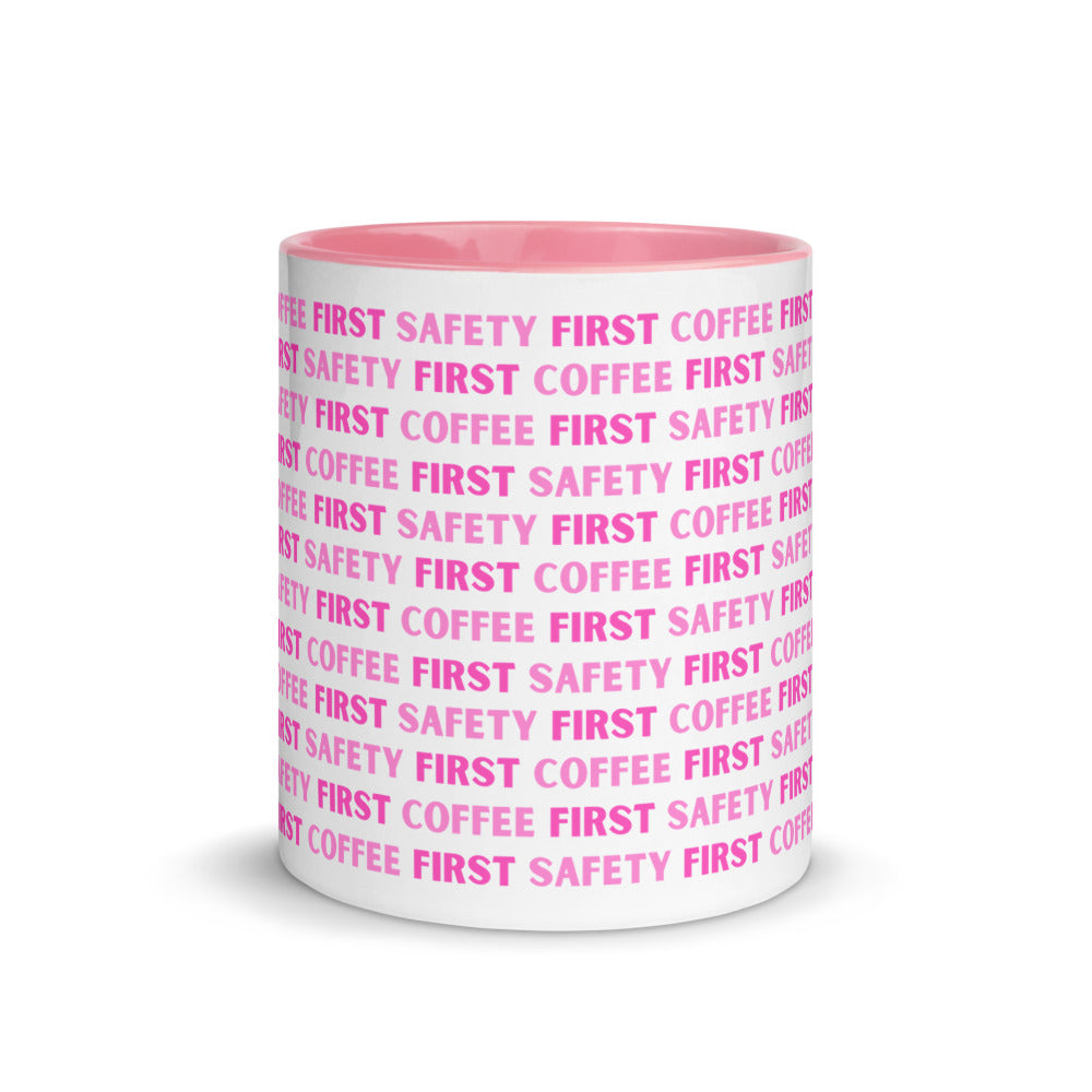 White ceramic mug with pink repeating text that says "Safety First, Coffee First" with a pink rim, inside, and handle.
