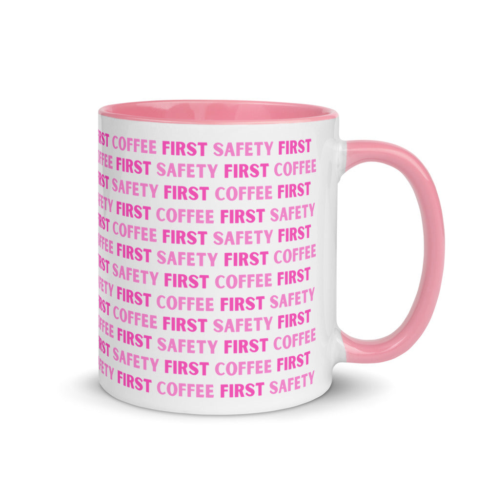 White ceramic mug with pink repeating text that says "Safety First, Coffee First" with a pink rim, inside, and handle.